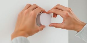 Hands installing a wireless home sensor on a wall.